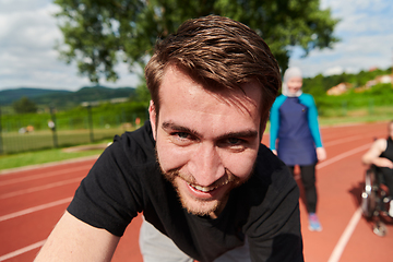 Image showing A portrait of a man with a Muslim woman and a woman in a wheelchair running on a marathon track in the background