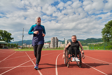 Image showing A Muslim woman in a burqa running together with a woman in a wheelchair on the marathon course, preparing for future competitions.