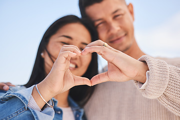 Image showing Love, heart hands and portrait of happy couple with blue sky, nature and holiday travel for summer. Care, marriage and smile, loving sign language emoji with man and woman on beach vacation together.