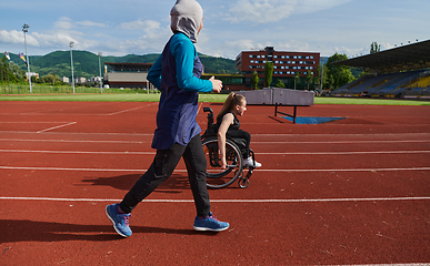 Image showing A Muslim woman in a burqa running together with a woman in a wheelchair on the marathon course, preparing for future competitions.