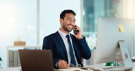 Image showing Happy business man talking on his phone while working on a computer and smiling alone at work. Young corporate professional having a discussion and explaining project details to a colleague or client