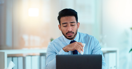 Image showing A modern business man feeling sick with covid fatigue while working online at a desk on his laptop. Closeup of an male corporate manager blowing his nose. An ill office worker frustrated at work.