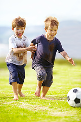 Image showing Having a friendly game. Two cute little boys playing soccer together outside while covered in mud.