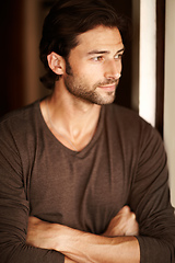 Image showing Content with his lot in life. A handsome young man gazing out of a window with his arms folded.