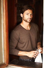 Image showing Long night ahead. Shot of a handsome young man drying off a glass while looking through a window.