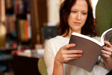 Image showing Immersed in the words. A young woman quietly reading a book while seated in a chair.