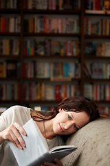 Image showing In her own world. An attractive young woman relaxing on a sofa with a book - copy space.
