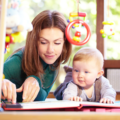 Image showing Look at this. Cute young mom lying alongside her infant son on the playroom floor.