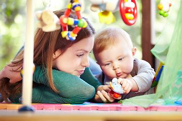 Image showing Filled with curiousity. Cute young mom lying alongside her infant son on the playroom floor.