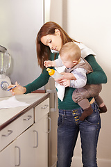 Image showing Being a mom is a real juggling act. Young mom trying to multi-task while holding her baby son and his bottle.