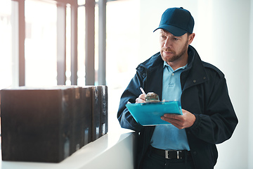 Image showing Making sure every delivery is signed and dated. Shot of a handsome delivery man writing on his clipboard while waiting in the lobby with a customers order.