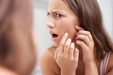 Image showing What A pimple. A young woman looking shocked as she examines her skin.