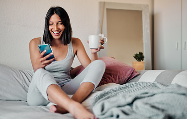 Image showing Mornings are for coffee and social media. Shot of a young woman using a smartphone and enjoying a cup of coffee in bed at home.