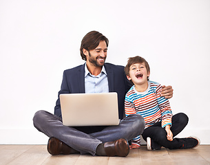 Image showing Enjoying some funny online videos. A father and son sitting on the floor with a laptop.