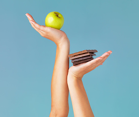 Image showing The healthy choice is in your hands. Cropped studio shot of a woman holding up chocolate and an apple against a blue background.