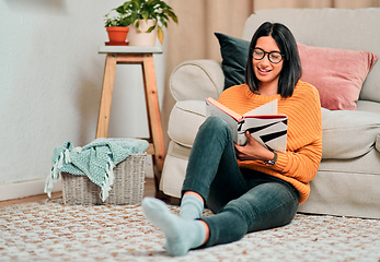 Image showing Nothing says relaxation like reading a good book. Shot of a young woman relaxing on the floor in the living room and reading a book at home.