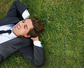 Image showing Just taking a breather. A young businessman lying down on green grass.