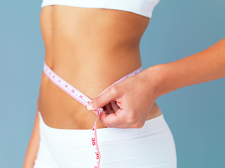 Image showing The proof is in the inches. Cropped studio shot of a fit young woman measuring her waist against a blue background.