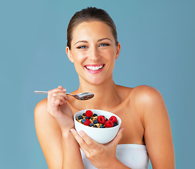 Image showing Healthiness and happiness go hand in hand. Studio shot of an attractive young woman eating a bowl of muesli and fruit against a blue background.