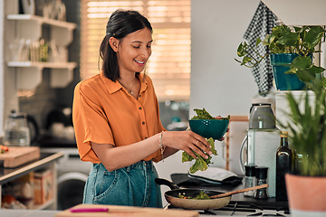 Image showing Leafy greens add goodness to any meal. Shot of a happy young woman preparing a healthy meal at home.