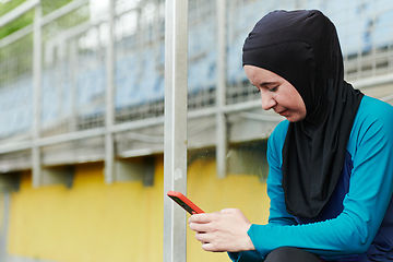 Image showing Muslim sports fitness woman dressed in hijab and dark clothes outdoors in green nature park using mobile phone chatting