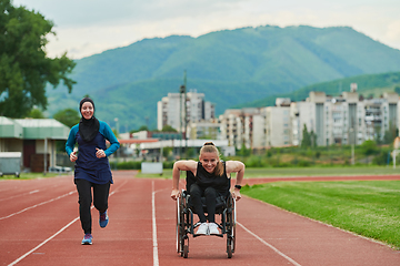 Image showing A Muslim woman in a burqa running together with a woman in a wheelchair on the marathon course, preparing for future competitions.