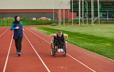 Image showing A Muslim woman in a burqa running together with a woman in a wheelchair on the marathon course, preparing for future competitions.