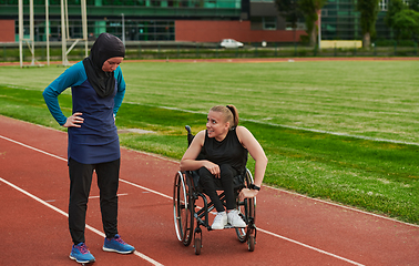 Image showing A Muslim woman wearing a burqa resting with a woman with disability after a hard training session on the marathon course