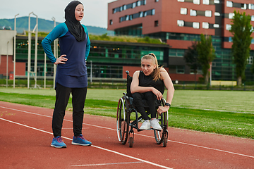 Image showing A Muslim woman wearing a burqa resting with a woman with disability after a hard training session on the marathon course