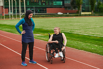 Image showing A Muslim woman wearing a burqa resting with a woman with disability after a hard training session on the marathon course