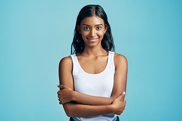 Image showing Confident and content. Studio portrait of a beautiful young woman standing with her arms crossed against a blue background.