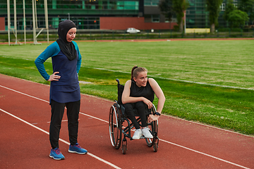 Image showing A Muslim woman wearing a burqa resting with a woman with disability after a hard training session on the marathon course