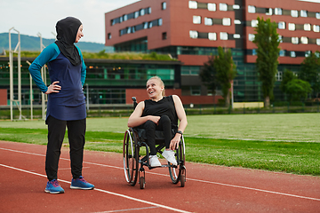 Image showing A Muslim woman wearing a burqa resting with a woman with disability after a hard training session on the marathon course