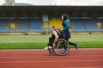 Image showing A Muslim woman in a burqa running together with a woman in a wheelchair on the marathon course, preparing for future competitions.