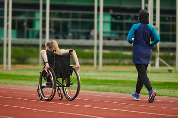 Image showing A Muslim woman in a burqa running together with a woman in a wheelchair on the marathon course, preparing for future competitions.