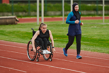 Image showing A Muslim woman in a burqa running together with a woman in a wheelchair on the marathon course, preparing for future competitions.