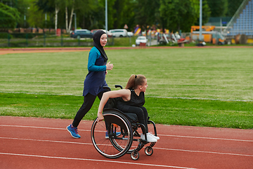 Image showing A Muslim woman in a burqa running together with a woman in a wheelchair on the marathon course, preparing for future competitions.