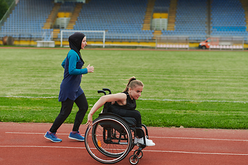 Image showing A Muslim woman in a burqa running together with a woman in a wheelchair on the marathon course, preparing for future competitions.