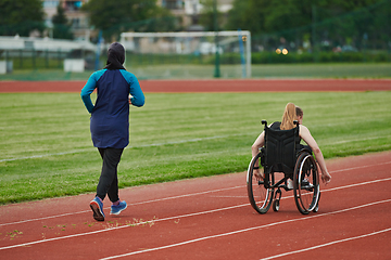 Image showing A Muslim woman in a burqa running together with a woman in a wheelchair on the marathon course, preparing for future competitions.