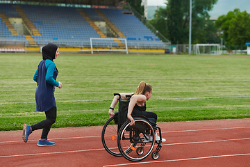 Image showing A Muslim woman in a burqa running together with a woman in a wheelchair on the marathon course, preparing for future competitions.