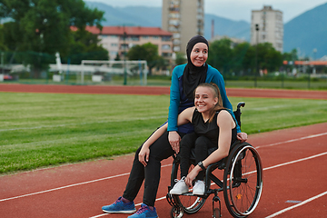 Image showing A Muslim woman wearing a burqa resting with a woman with disability after a hard training session on the marathon course