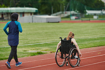 Image showing A Muslim woman in a burqa running together with a woman in a wheelchair on the marathon course, preparing for future competitions.