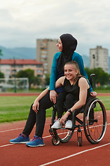 Image showing A Muslim woman wearing a burqa resting with a woman with disability after a hard training session on the marathon course