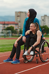 Image showing A Muslim woman wearing a burqa resting with a woman with disability after a hard training session on the marathon course