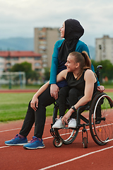 Image showing A Muslim woman wearing a burqa resting with a woman with disability after a hard training session on the marathon course