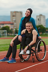 Image showing A Muslim woman wearing a burqa resting with a woman with disability after a hard training session on the marathon course