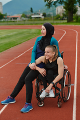 Image showing A Muslim woman wearing a burqa resting with a woman with disability after a hard training session on the marathon course