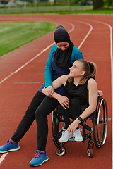 Image showing A Muslim woman wearing a burqa resting with a woman with disability after a hard training session on the marathon course