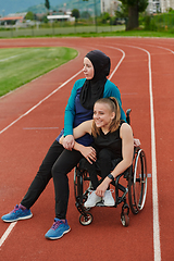 Image showing A Muslim woman wearing a burqa resting with a woman with disability after a hard training session on the marathon course