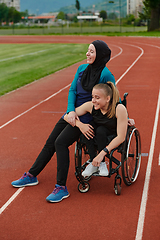 Image showing A Muslim woman wearing a burqa resting with a woman with disability after a hard training session on the marathon course